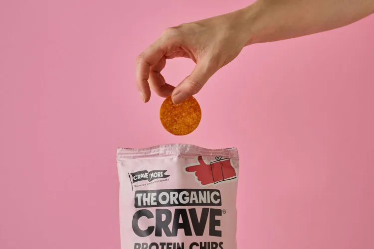 Hand placing a protein chip into a flexible snack packaging bag